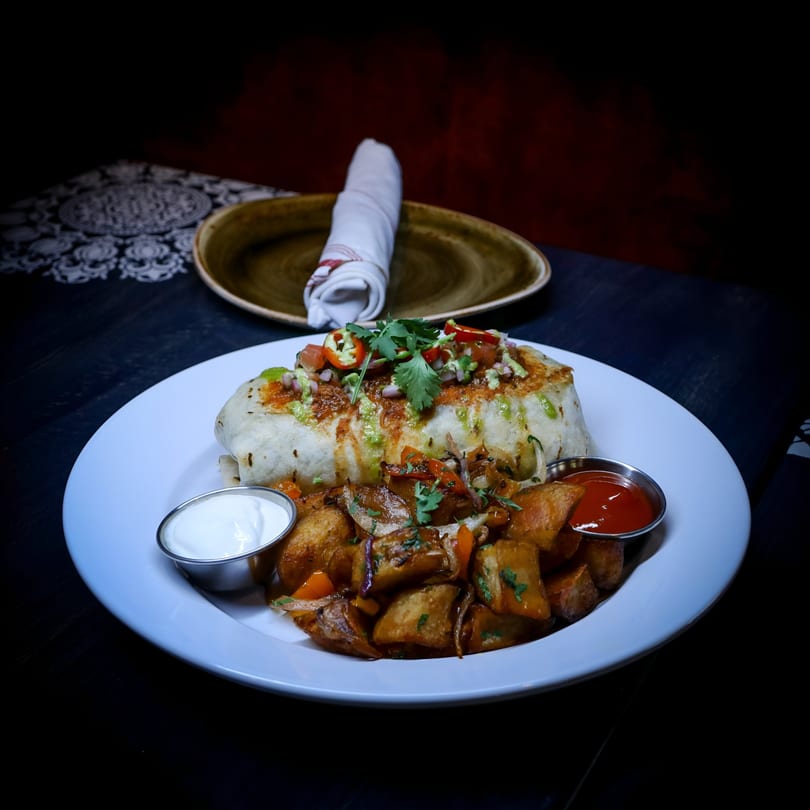 A V 14 Street Lounge burrito with salsa, guacamole, and cilantro, served with roasted potatoes and sauces.