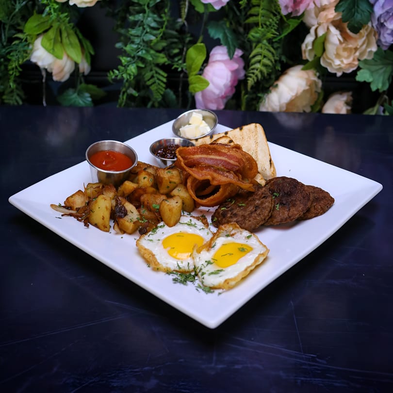 A New American breakfast plate with fried eggs, bacon, sausage, home fries, and toast.