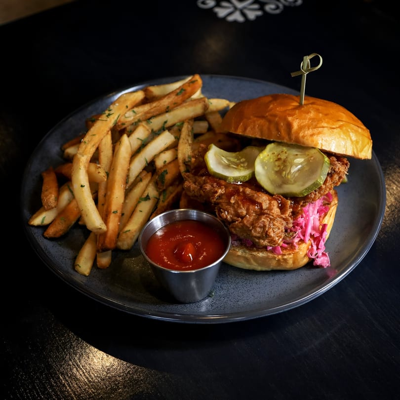 A fried chicken sandwich with pickles, red cabbage, and a side of fries and ketchup.