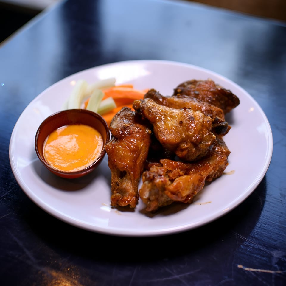 A plate of glazed chicken wings with a side of celery, carrots, and dipping sauce.