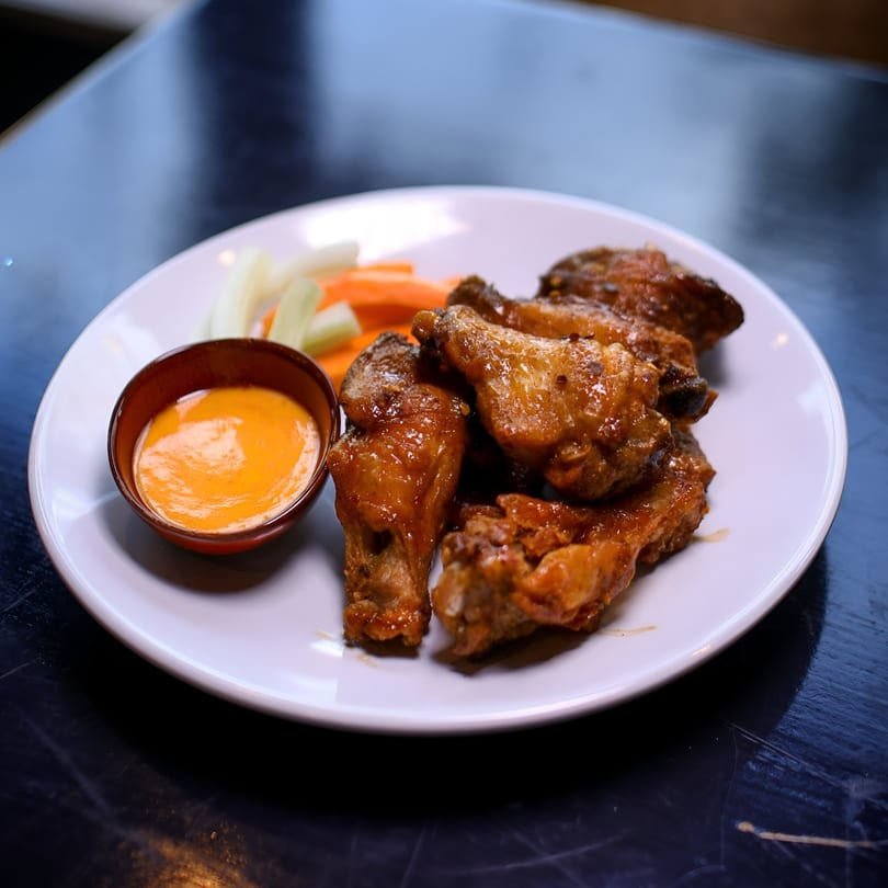 A plate of glazed chicken wings with a side of celery, carrots, and dipping sauce.